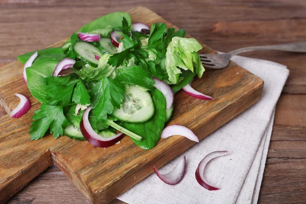 Mezclar hojas de ensalada con pepino en rodajas y cebolla sobre tabla de cortar y fondo de mesa de madera —  Fotos de Stock
