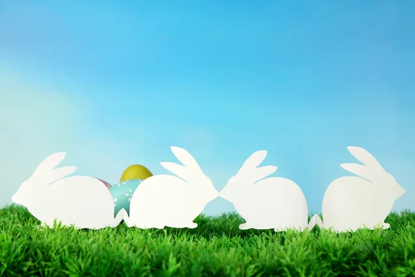 Papel Conejos de Pascua y huevos sobre hierba verde, sobre fondo de cielo —  Fotos de Stock