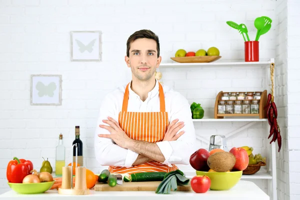 Uomo a tavola con diversi prodotti e utensili in cucina su sfondo bianco a parete — Foto Stock