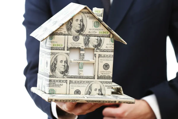 Model van huis gemaakt van geld in mannenhand geïsoleerd op witte achtergrond — Stockfoto