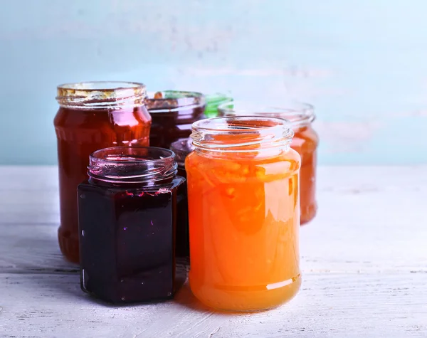 Frascos caseros de mermelada de frutas sobre mesa de madera y fondo de pared de color — Foto de Stock