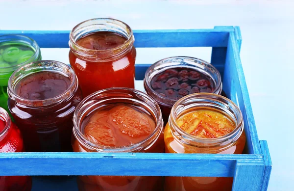 Zelfgemaakte potten van vruchten jam in krat op kleur muur tabelachtergrond — Stockfoto