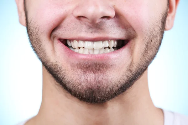 Улыбающийся молодой человек после посещения стоматолога на ярком размытом фоне — стоковое фото
