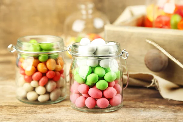 Multicolor candies in glass jars on wooden background — Stock Photo, Image