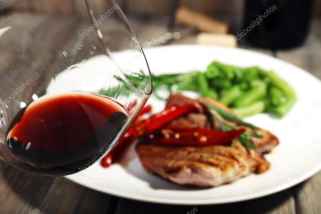 Glass of wine and steak with vegetables on plate on wooden background