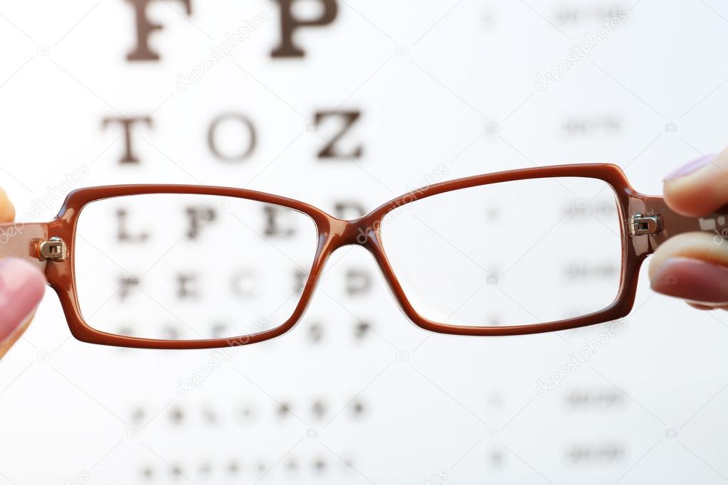 Eye glasses in female hands on eyesight test chart background