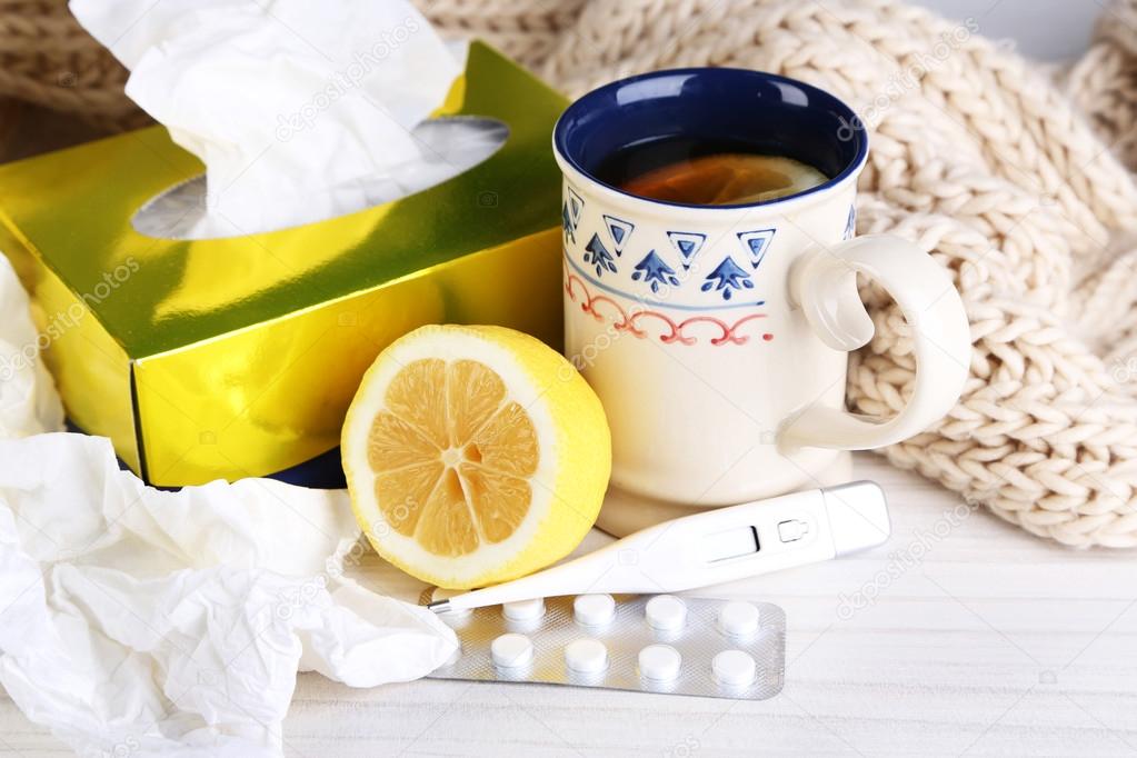 Hot tea for colds, pills and handkerchiefs on table close-up