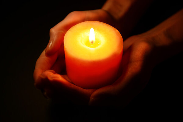 Candle in female hands on black background
