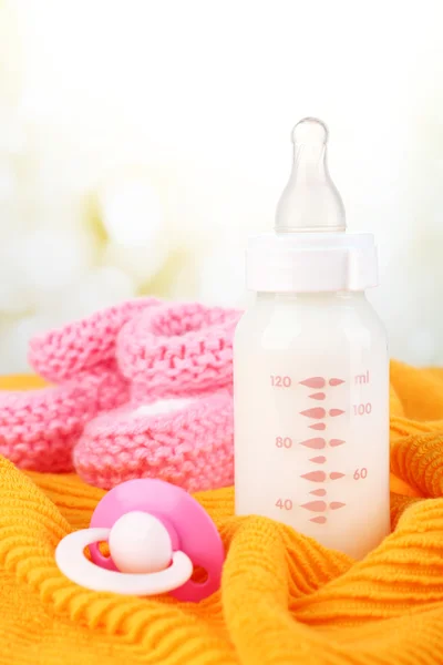 Baby milk bottle, pacifier and babys bootees on yellow background — Stock Photo, Image