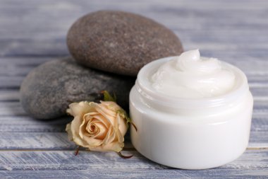 Spa taşlı kozmetik krem ve ahşap arka planda gül