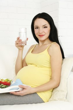 Genç hamile kadın kanepe ile su ve salata eve iç arka plan üzerinde rahatlatıcı