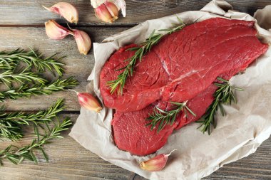 Biberiye ve sarımsak ahşap arka plan üzerinde kağıt üzerinde ham sığır eti biftek