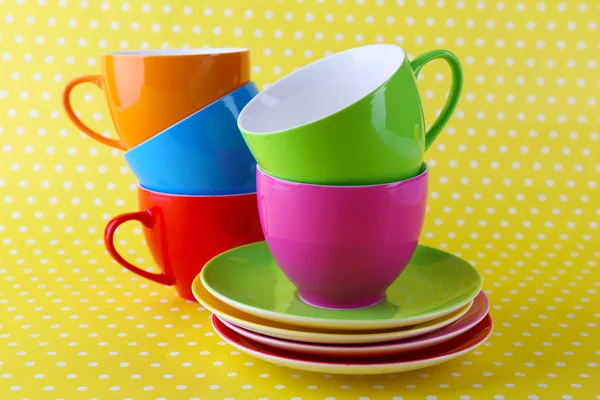 Tazze colorate e piattini su sfondo colore — Foto Stock