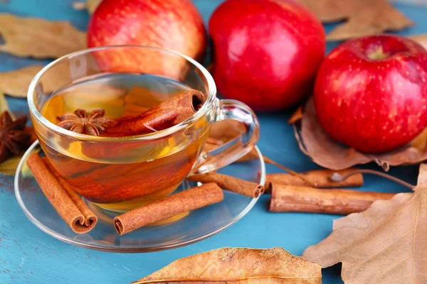 Sammansättningen av äppelcider med kanelstänger, färska röda äpplen och höstlöv på trä bakgrund — Stockfoto