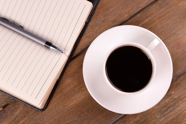 Tasse Kaffee auf Untertasse mit Tagebuch und Stift auf Holztischhintergrund — Stockfoto