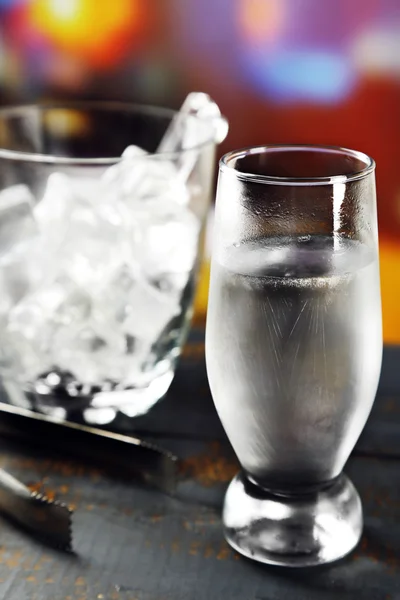 Vaso de agua con hielo sobre mesa de madera y fondo borroso brillante — Foto de Stock
