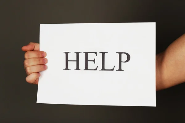 Sheet of paper with Help sign in male hand on dark background — Stock Photo, Image