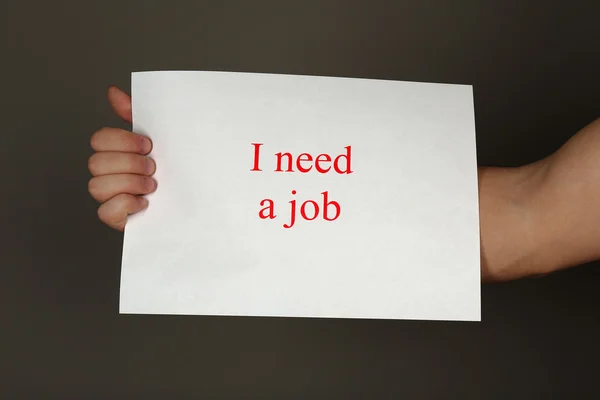 Sheet of paper with inscription I need a job in male hand on dark background — Stock Photo, Image