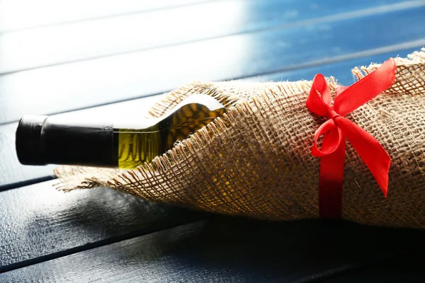 Wine bottle wrapped in burlap cloth on color wooden planks background — Stock Photo, Image