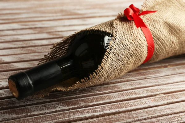 Bouteille de vin enveloppée dans un tissu de toile de jute sur des planches en bois — Photo
