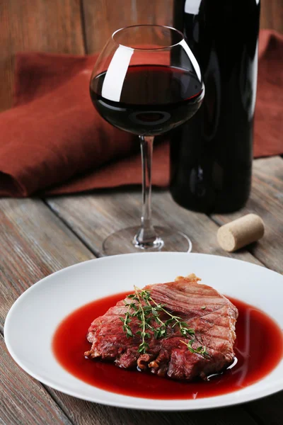 Grilled steak in wine sauce with glass of wine on wooden background