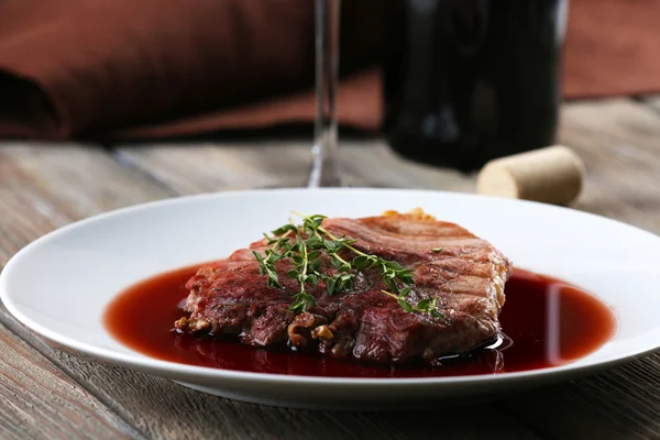 Bife grelhado em molho de vinho com garrafa de vinho em fundo de madeira — Fotografia de Stock