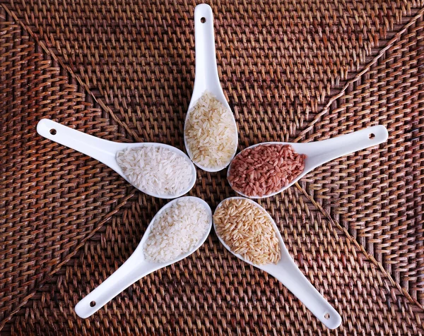 Diferentes tipos de arroz en cucharas sobre fondo de mimbre — Foto de Stock