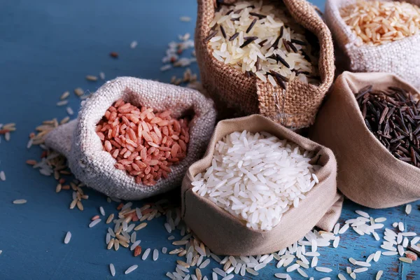 Diferentes tipos de arroz em sacos no fundo de madeira — Fotografia de Stock