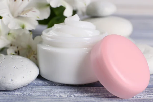 Crema cosmética con flores y piedras de spa sobre fondo de madera — Foto de Stock