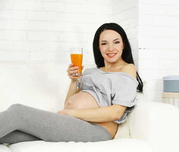 Jovem grávida relaxante no sofá com vidro de suco em casa interior fundo — Fotografia de Stock