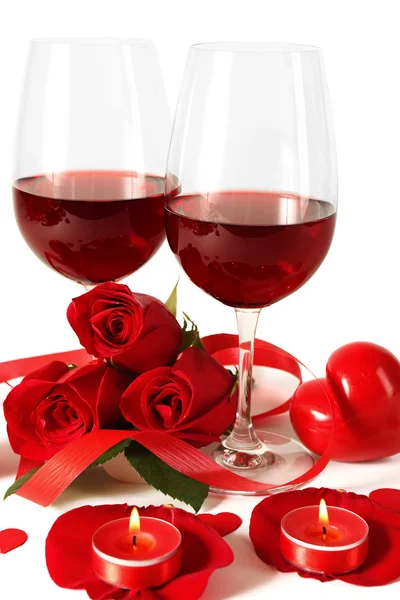 Komposition med rött vin i glasen, röda rosor, band och dekorativa hjärtan på ljus bakgrund — Stockfoto