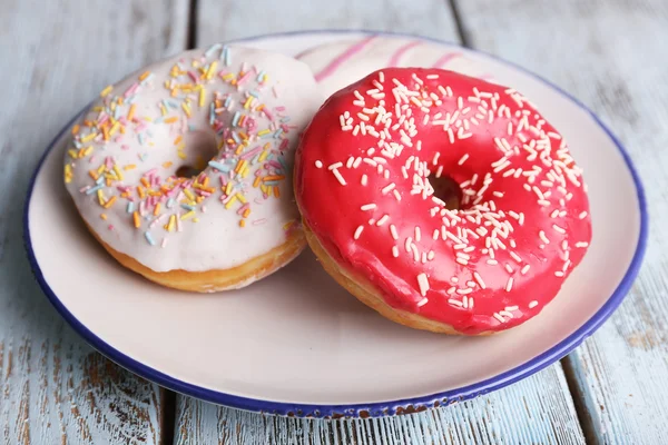 Delicious donuts with icing on plate on wooden background — Stock Photo, Image