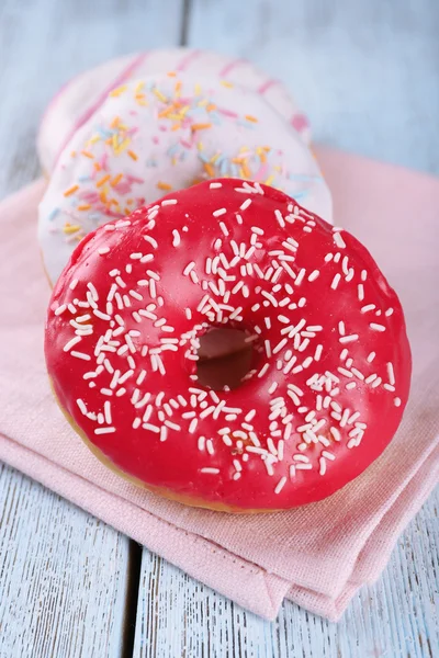 Delicious donuts with icing on napkin on wooden background — Stock Photo, Image