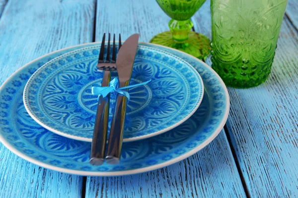 Pusty kolorowy talerz, szklanki i srebrne naczynia na drewnianym stole — Zdjęcie stockowe