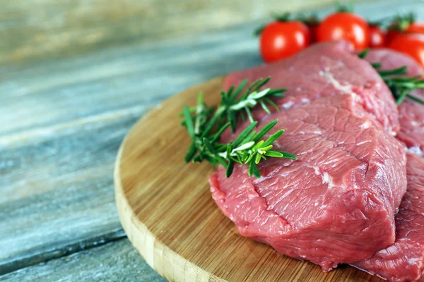 Filete de ternera crudo con romero y tomates cherry sobre tabla de cortar sobre fondo de madera —  Fotos de Stock