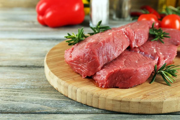 Raw beef steak on cutting board with vegetables and spices on wooden background — Stock Photo, Image