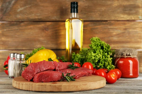 Raw beef steak on cutting board with vegetables and spices on wooden background