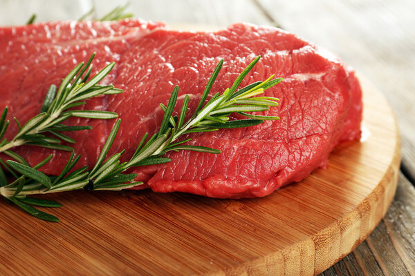 Raw beef steak with rosemary on cutting board on wooden background
