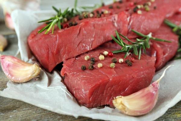 Syrové hovězí steak s rozmarýnem a česnekem na papíře o dřevěné pozadí — Stock fotografie