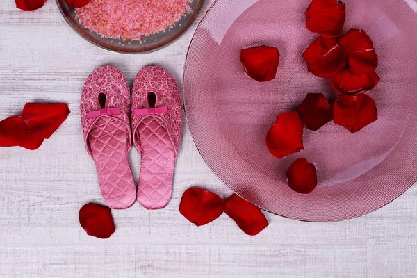 Spa bowl with water, rose petals, towel and slippers on light background. Concept of pedicure or natural spa treatment — Stock Photo, Image