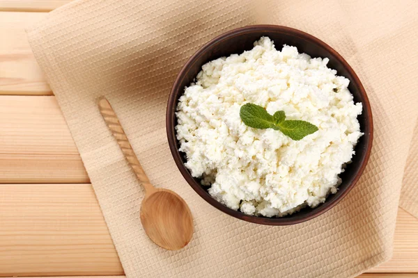 Cottage cheese in bowl with spoon on napkin on wooden background — Stock Photo, Image