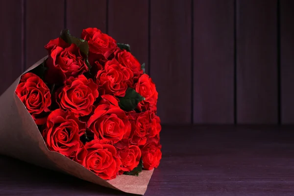 Bouquet de roses rouges enveloppé dans du papier sur fond de bois — Photo