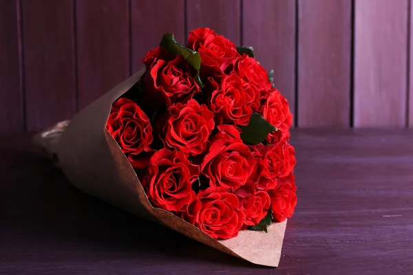 Bouquet of red roses wrapped in paper on wooden background — Stock Photo, Image