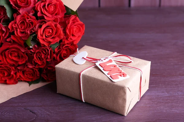 Ramo de rosas rojas envueltas en papel y caja de regalo sobre fondo de madera —  Fotos de Stock