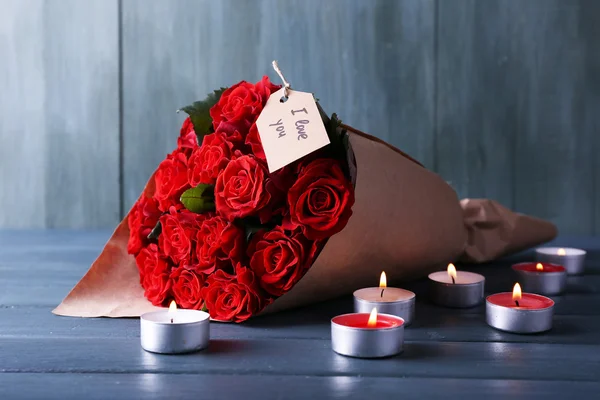 Ramo de rosas rojas con etiqueta envuelta en papel y velas sobre fondo de madera — Foto de Stock