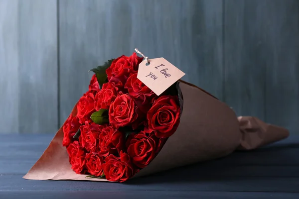 Bouquet of red roses with tag wrapped in paper on wooden background — Stock Photo, Image