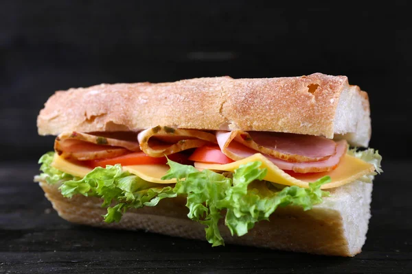 Свежий и вкусный сэндвич с ветчиной и овощами на деревянном фоне — стоковое фото