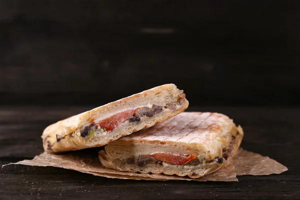 Fresh and tasty sandwiches on paper on wooden background — Stock Photo, Image