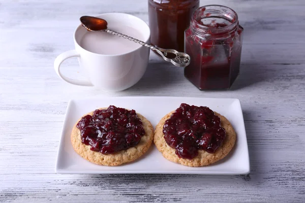 Delicious cookies with jam on plate and cup of coffee on wooden background — Stock Photo, Image