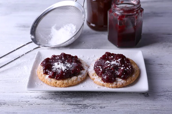 Deliciosas galletas con mermelada y azúcar en polvo en plato sobre fondo de madera — Foto de Stock